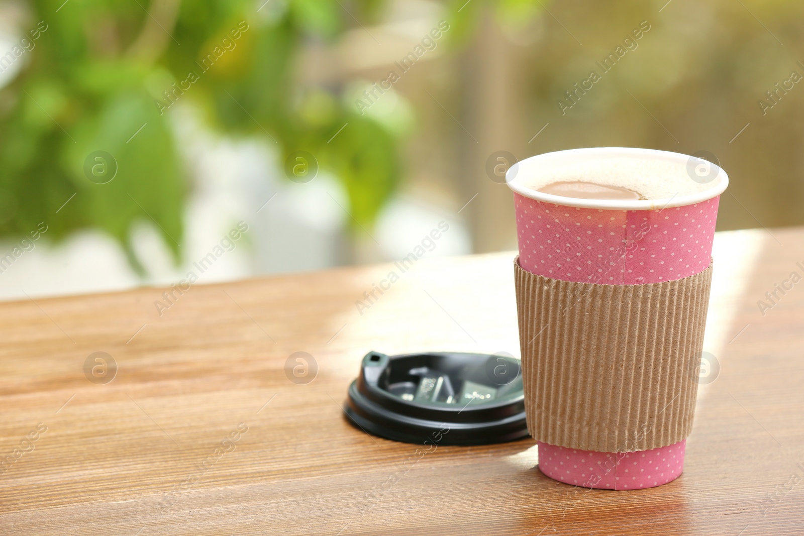 Photo of Cardboard cup of coffee on table against blurred background. Space for text