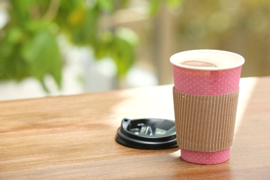 Photo of Cardboard cup of coffee on table against blurred background. Space for text