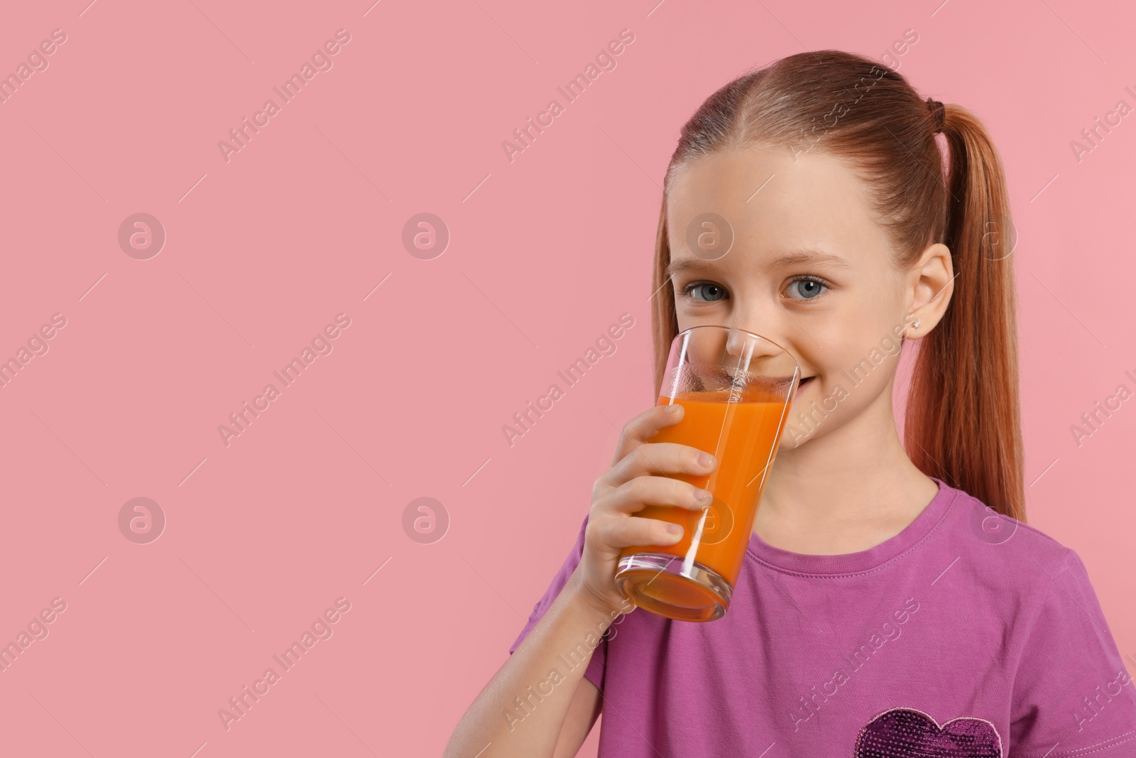 Photo of Cute little girl drinking fresh juice on pink background, space for text