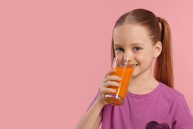Cute little girl drinking fresh juice on pink background, space for text