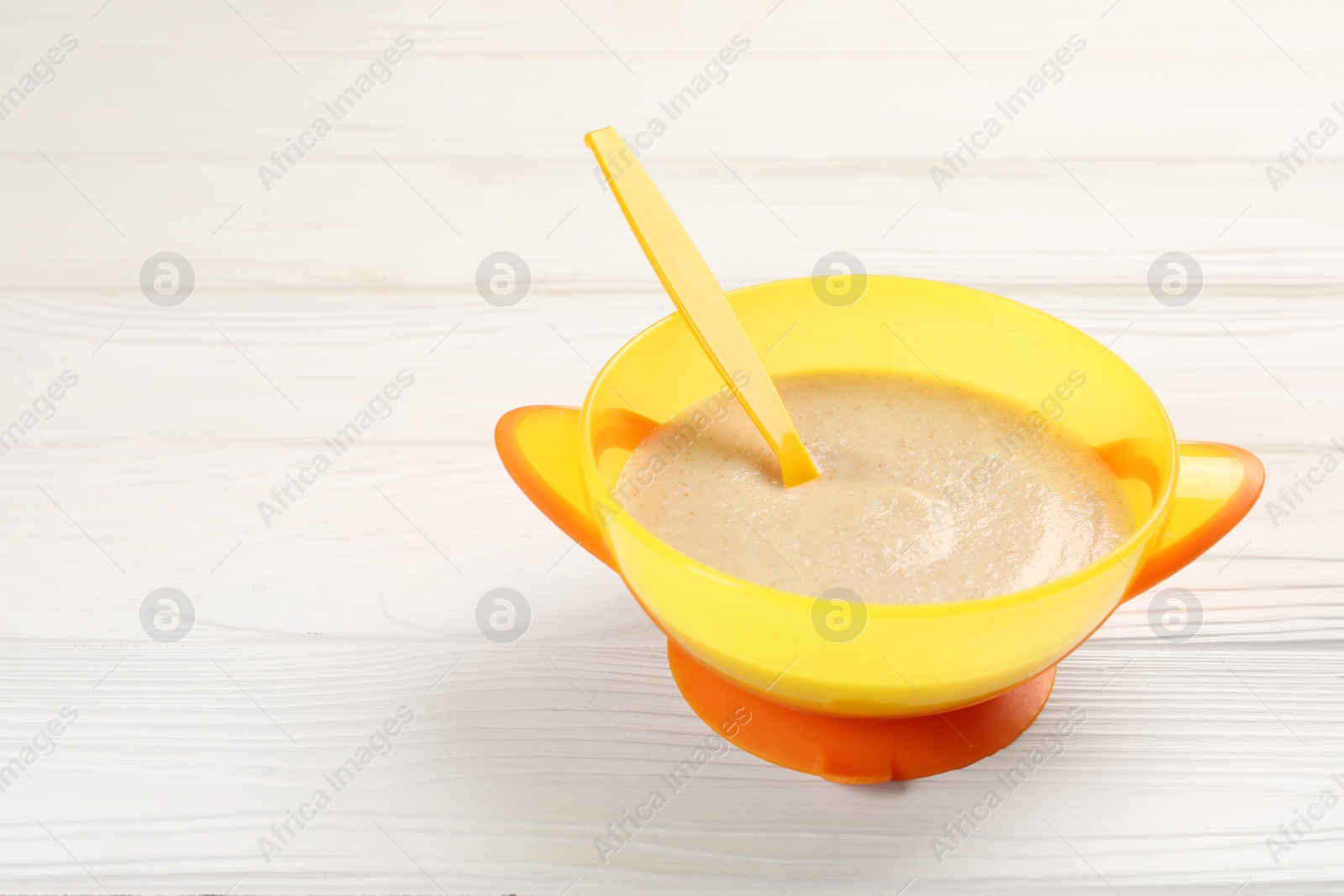 Photo of Baby food. Puree and spoon in bowl on white wooden table. Space for text