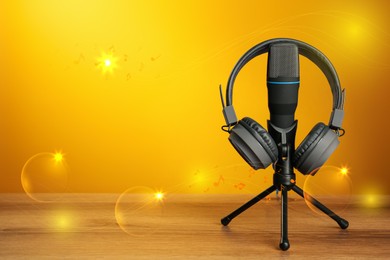 Image of Modern headphones and microphone with illustration musical notes on wooden table against orange background. Space for text