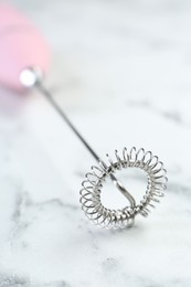 Pink milk frother wand on white marble table, closeup