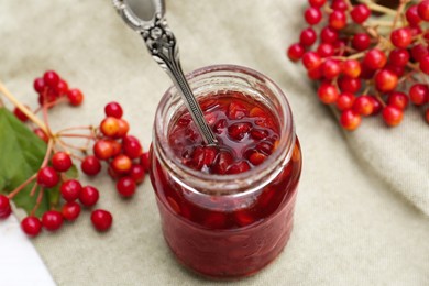 Photo of Jar with spoon and tasty viburnum jam on table