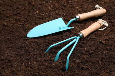 Photo of Metal gardening trowel and rake on fertile soil