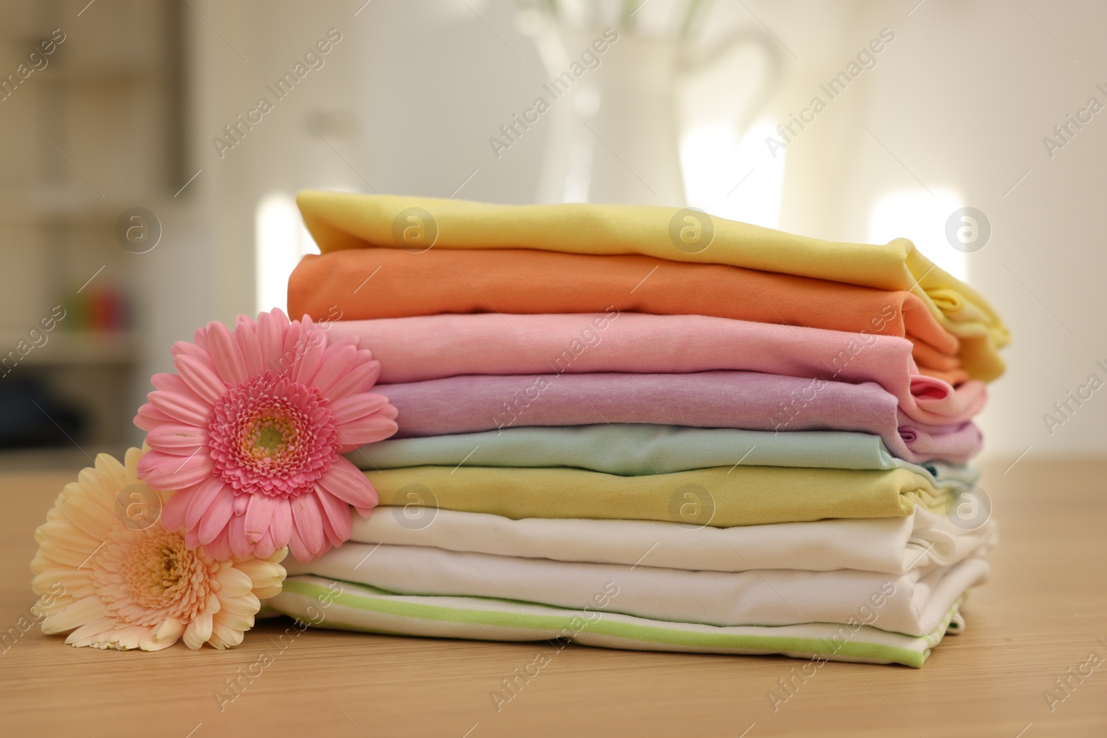 Photo of Stack of clean clothes and flowers on wooden table