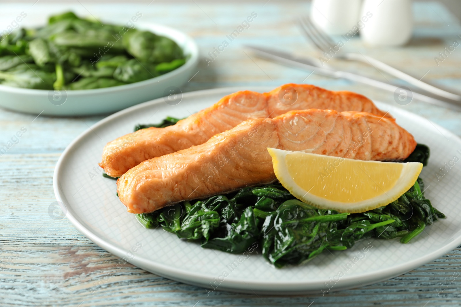 Photo of Tasty salmon with spinach and lemon on wooden table, closeup