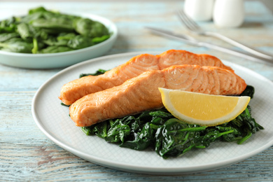 Photo of Tasty salmon with spinach and lemon on wooden table, closeup