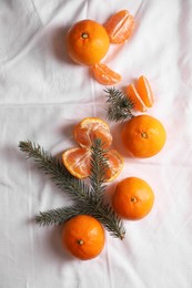 Photo of Delicious ripe tangerines and fir branches on white bedsheet, flat lay