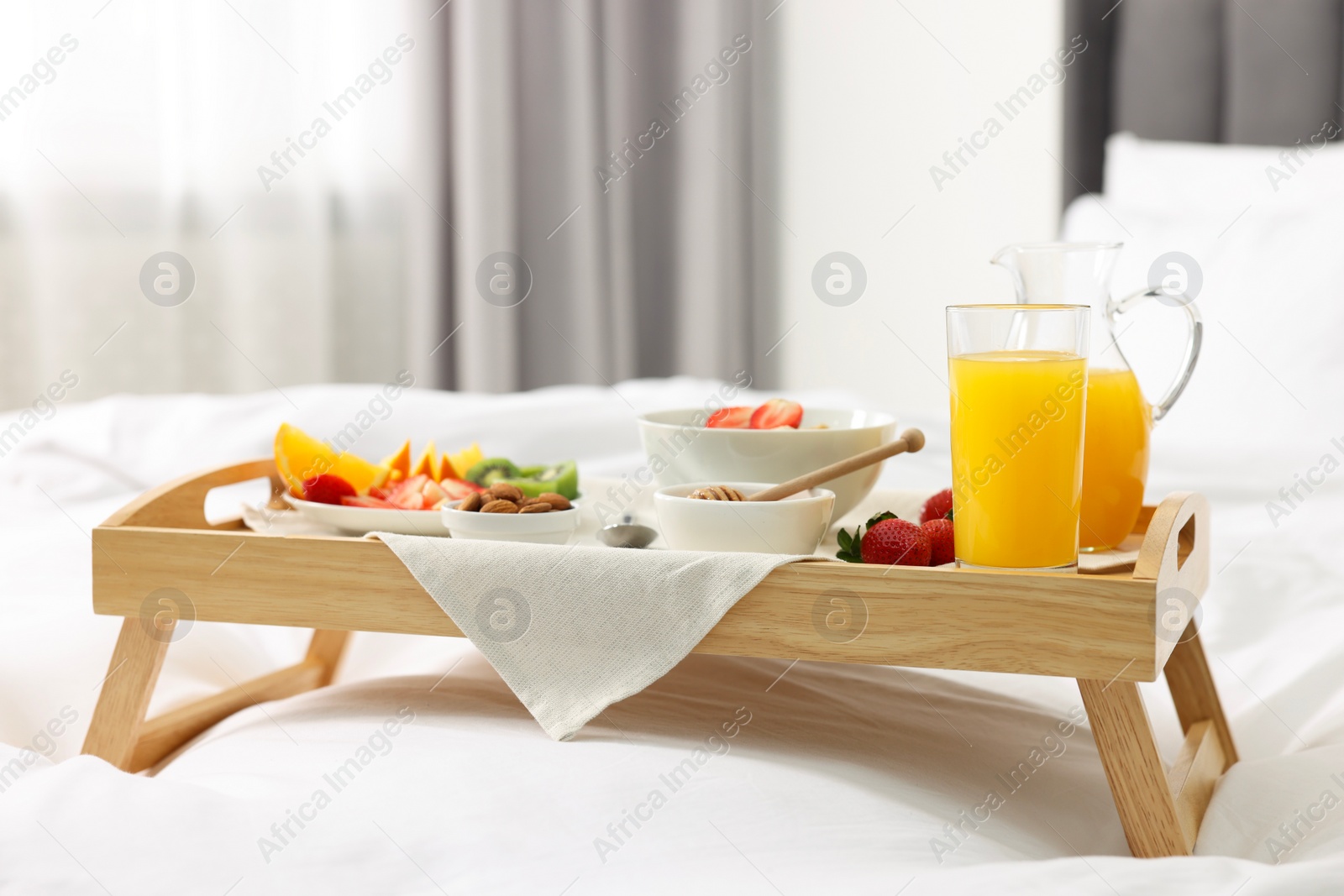 Tasty breakfast served in bed. Oatmeal, juice, fruits, almonds and honey on wooden tray Photo of Tasty breakfast served in bed. Oatmeal, juice, fruits, almonds and honey on wooden tray