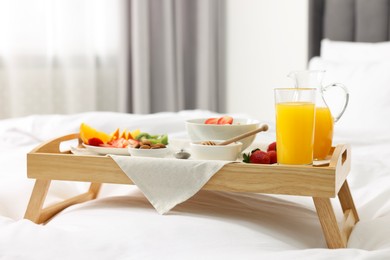 Photo of Tasty breakfast served in bed. Oatmeal, juice, fruits, almonds and honey on wooden tray