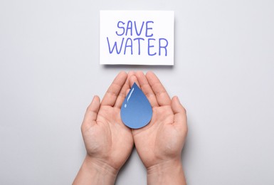 Photo of Man holding paper drop near card with words Save Water on light grey background, top view
