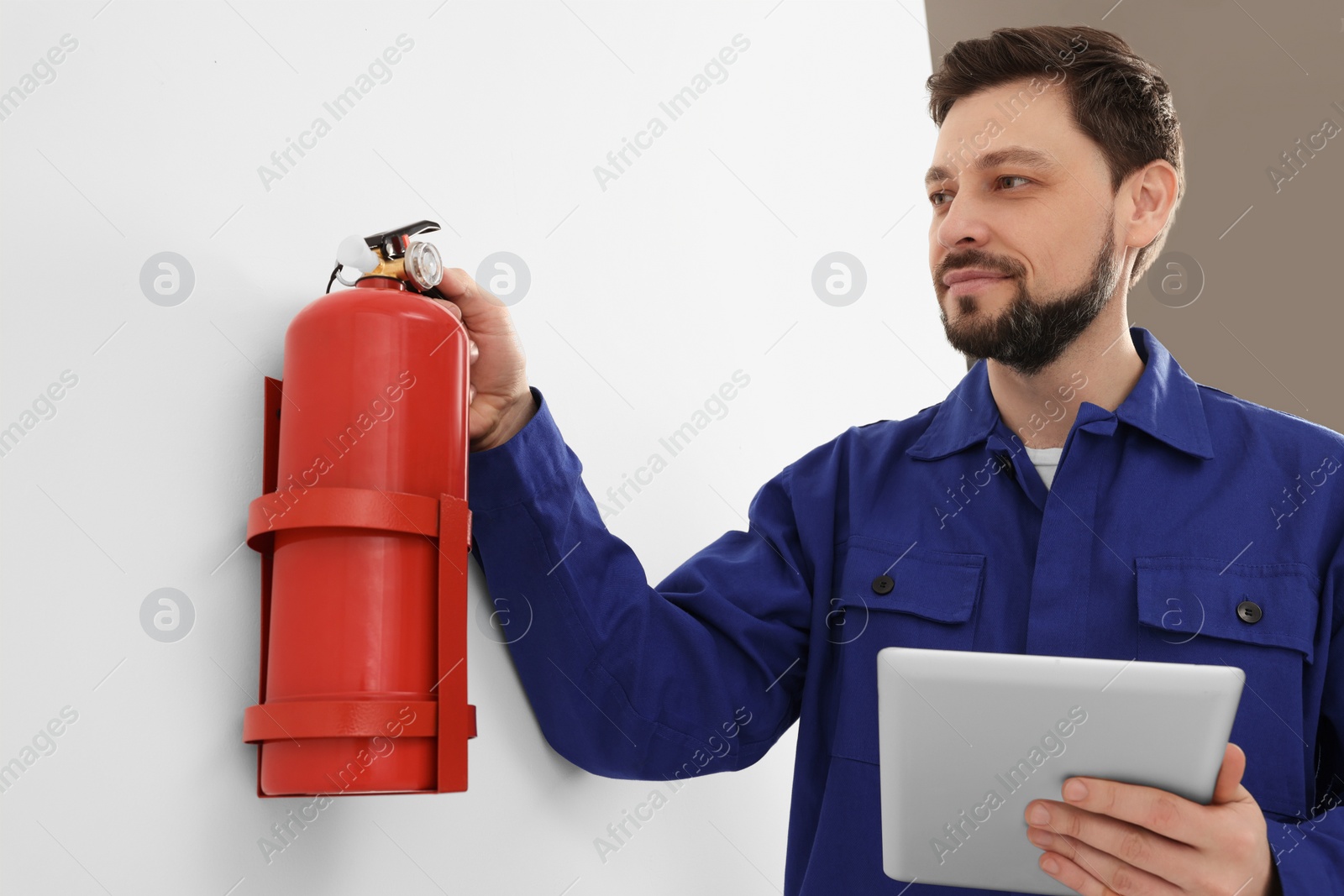 Photo of Man with tablet checking fire extinguisher indoors