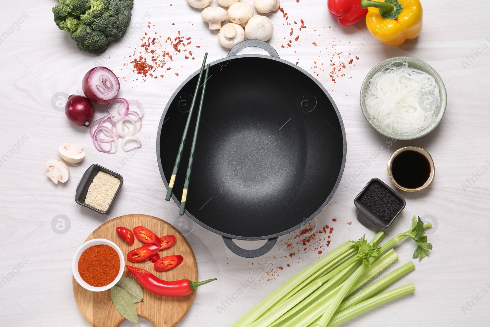 Photo of Wok, chopsticks and different products on white wooden table, flat lay