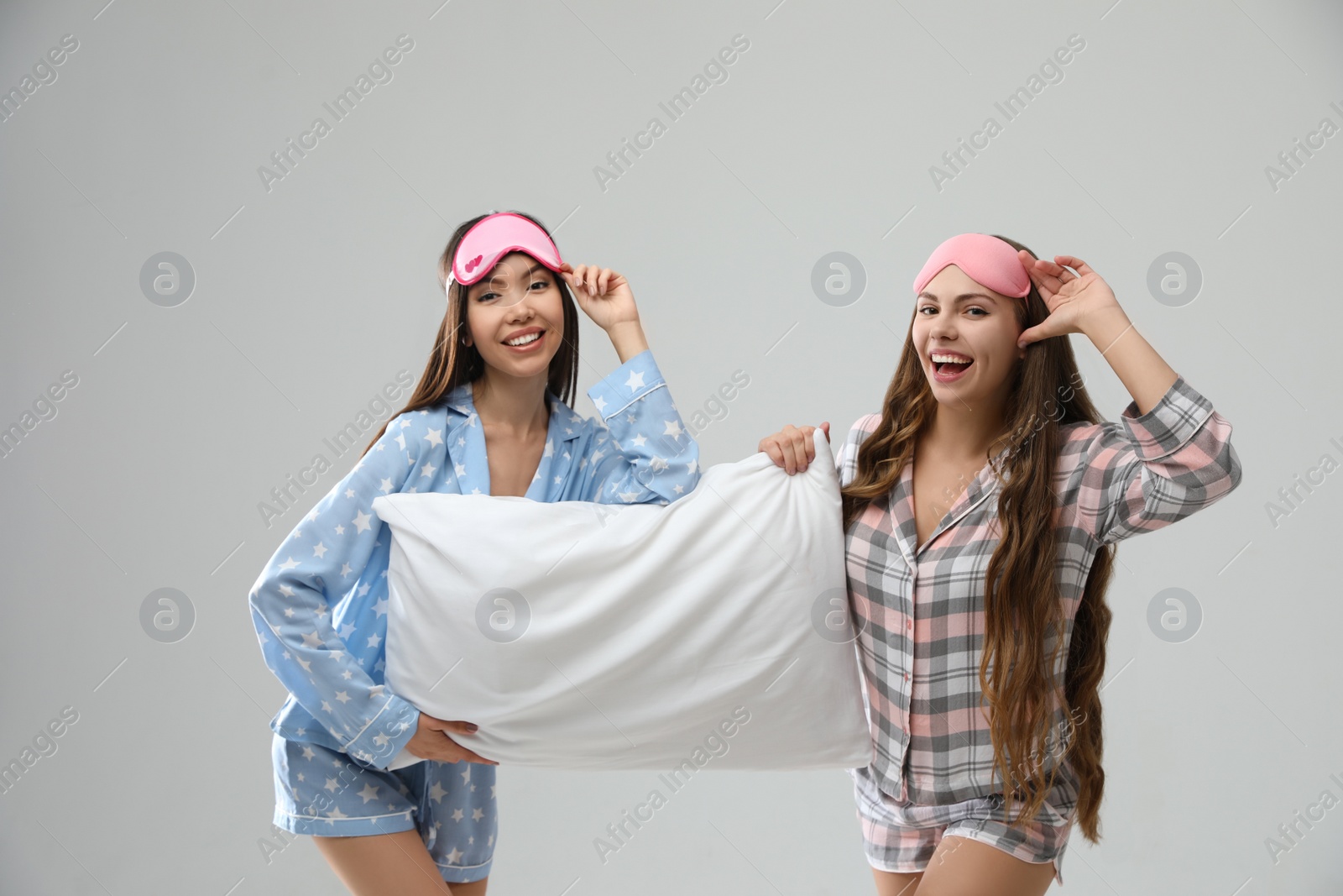 Photo of Beautiful women in pajamas with pillow on light grey background. Bedtime