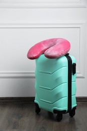 Photo of Pink travel pillow on turquoise suitcase indoors