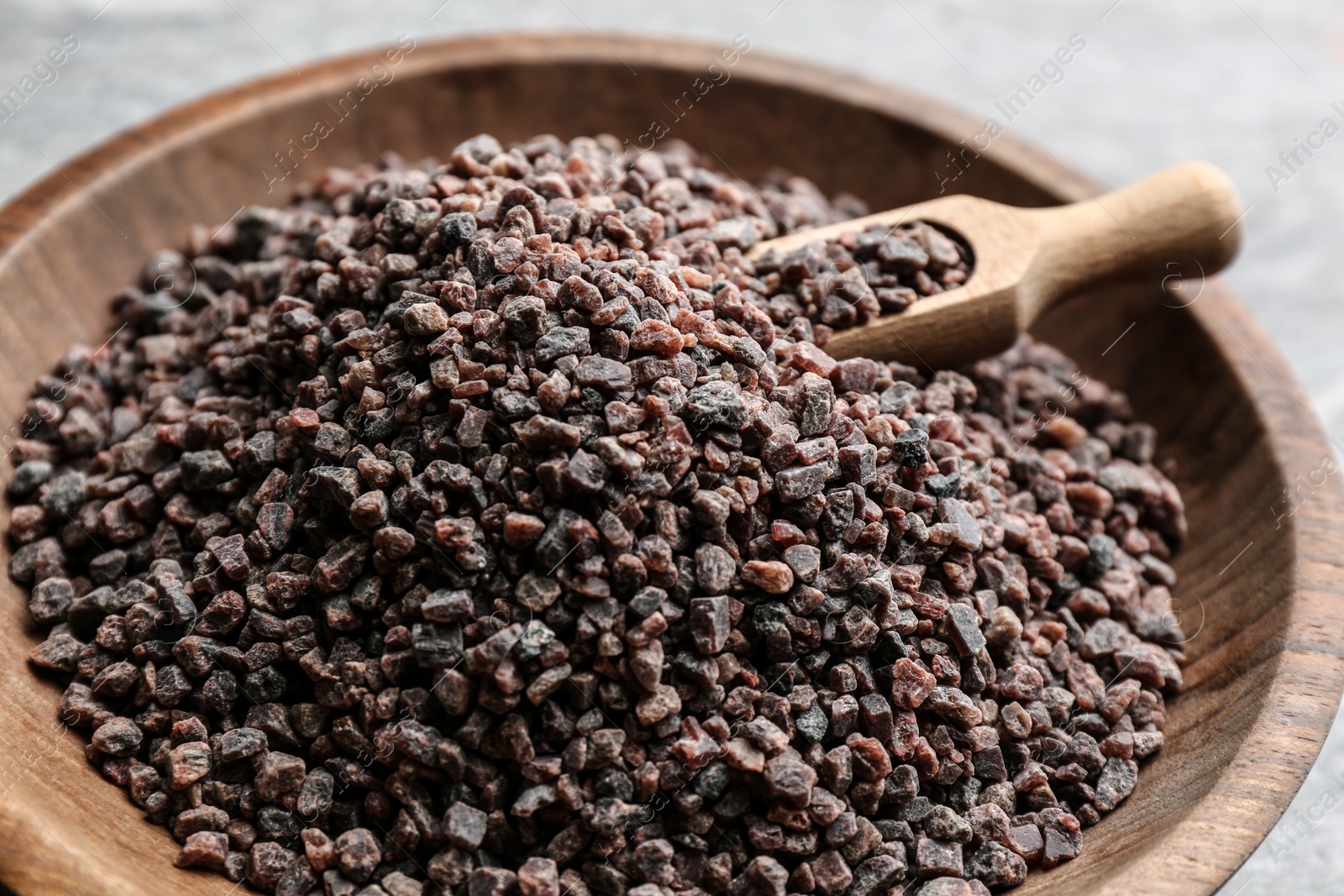 Photo of Black salt in wooden bowl with scoop, closeup