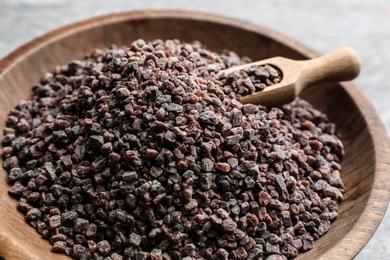 Black salt in wooden bowl with scoop, closeup