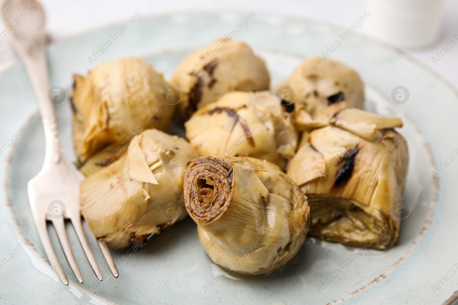 Photo of Delicious pickled artichokes and fork on plate, closeup
