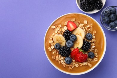 Photo of Delicious smoothie bowl with fresh berries, banana and oatmeal on violet background, flat lay. Space for text