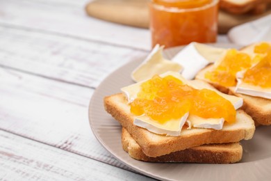 Tasty sandwiches with brie cheese and apricot jam on white wooden table, closeup. Space for text