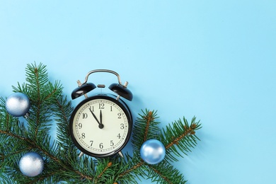 Alarm clock and decorated fir branch on light blue background, flat lay with space for text. New Year countdown
