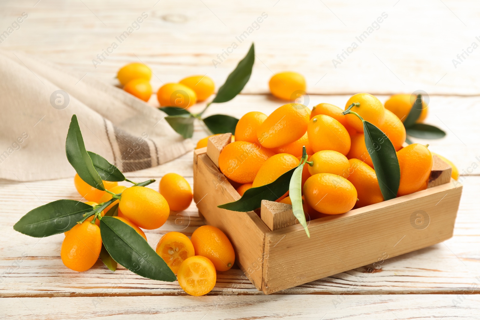 Photo of Fresh ripe kumquats in crate on white wooden table