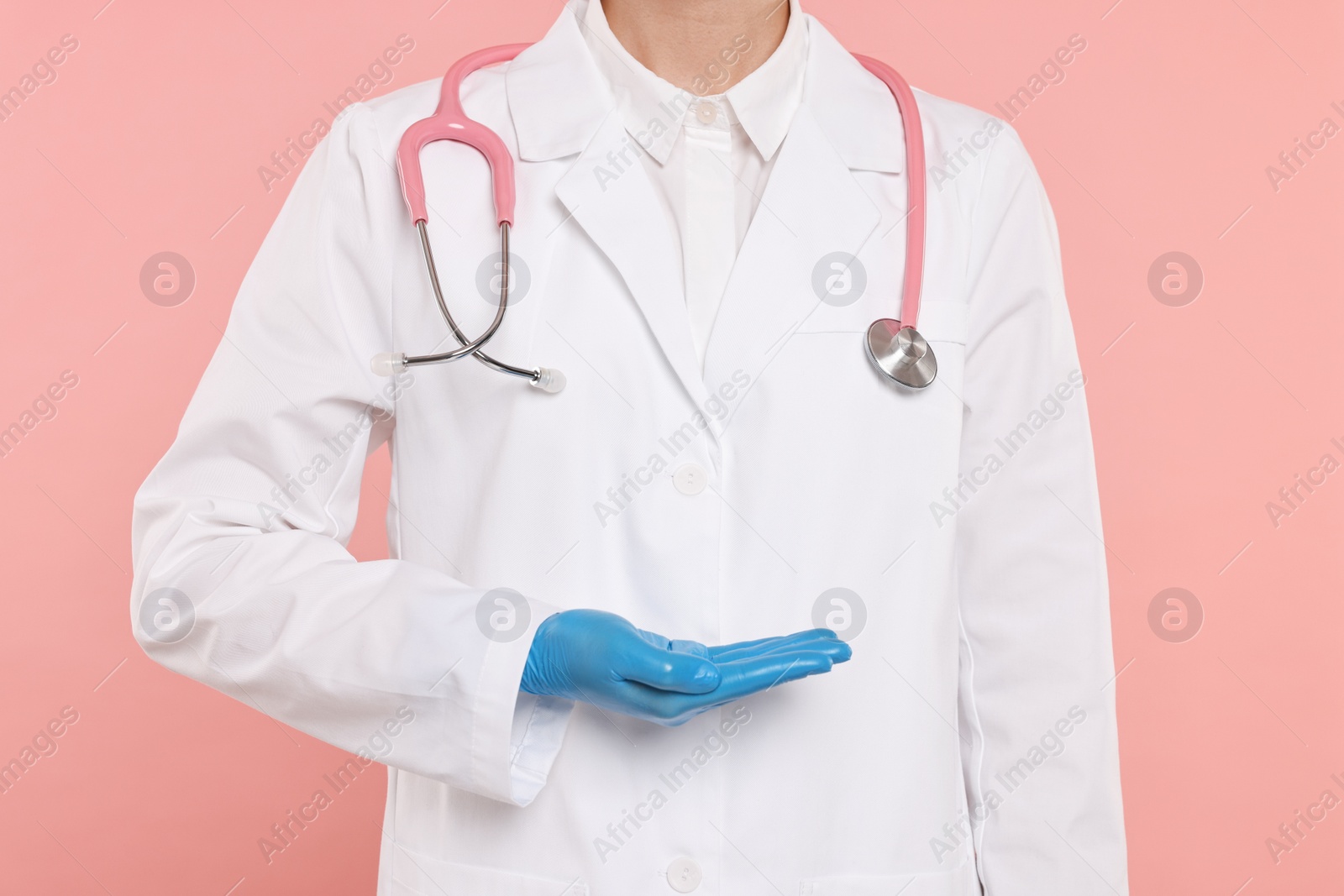 Photo of Doctor with stethoscope holding something on pink background, closeup