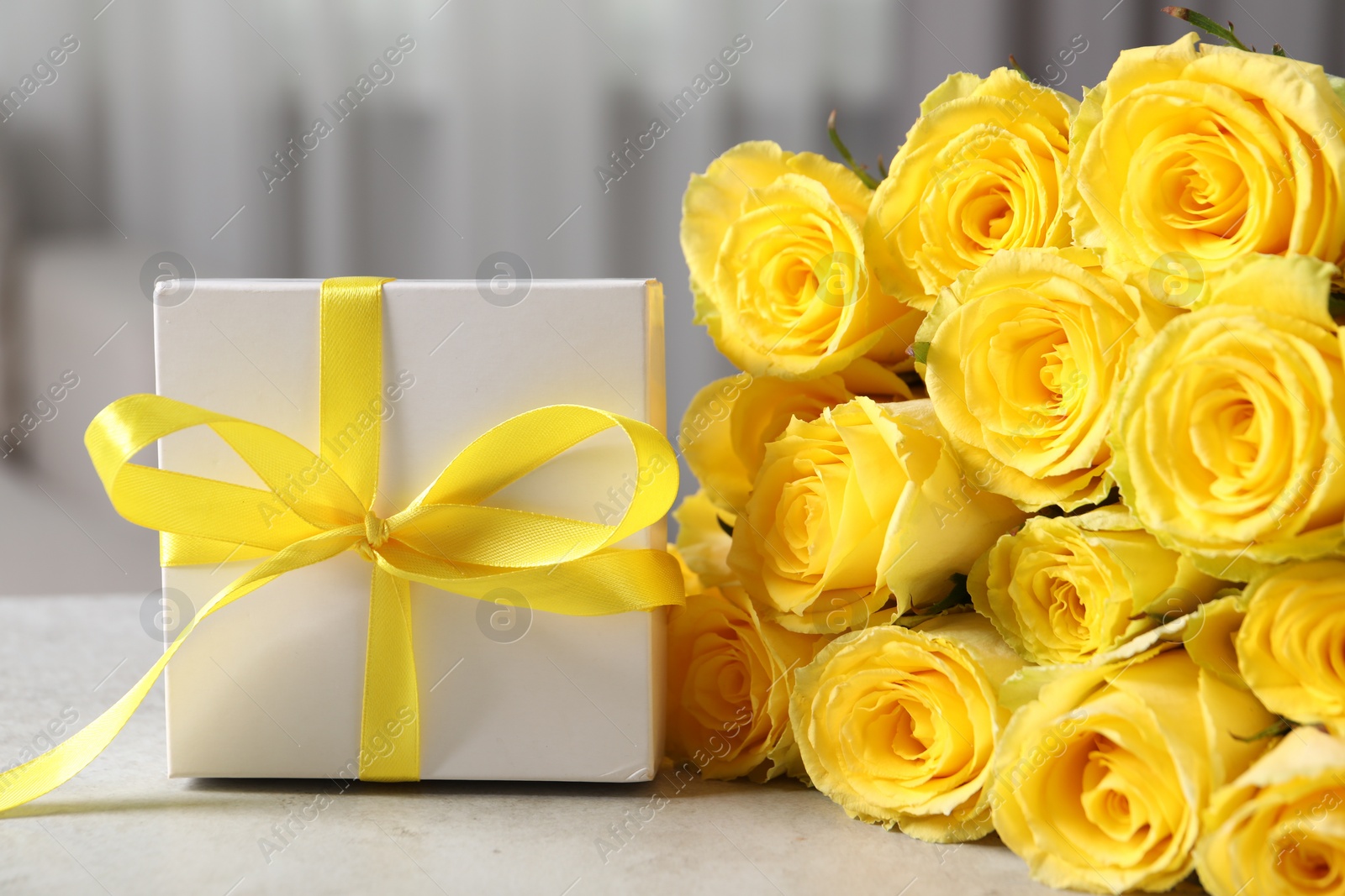 Photo of Beautiful bouquet of yellow roses and gift box on light grey table, closeup