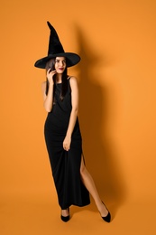 Beautiful woman wearing witch costume for Halloween party on yellow background