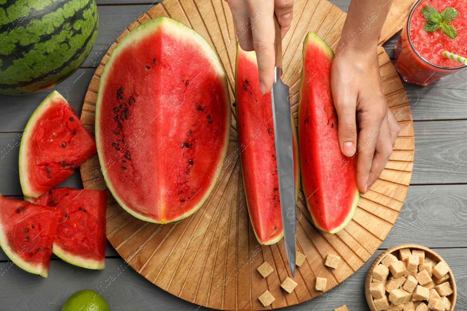 Photo of Woman cutting delicious watermelon at grey wooden table, top view