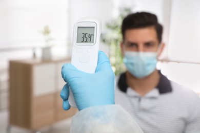 Photo of Doctor measuring man's temperature in office, closeup. Prevent spreading of Covid-19