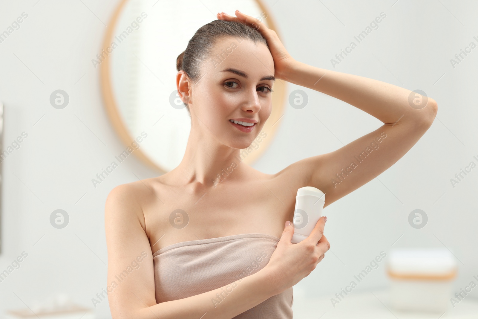 Photo of Beautiful young woman applying deodorant in bathroom