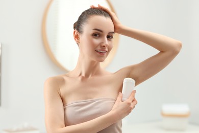 Beautiful young woman applying deodorant in bathroom