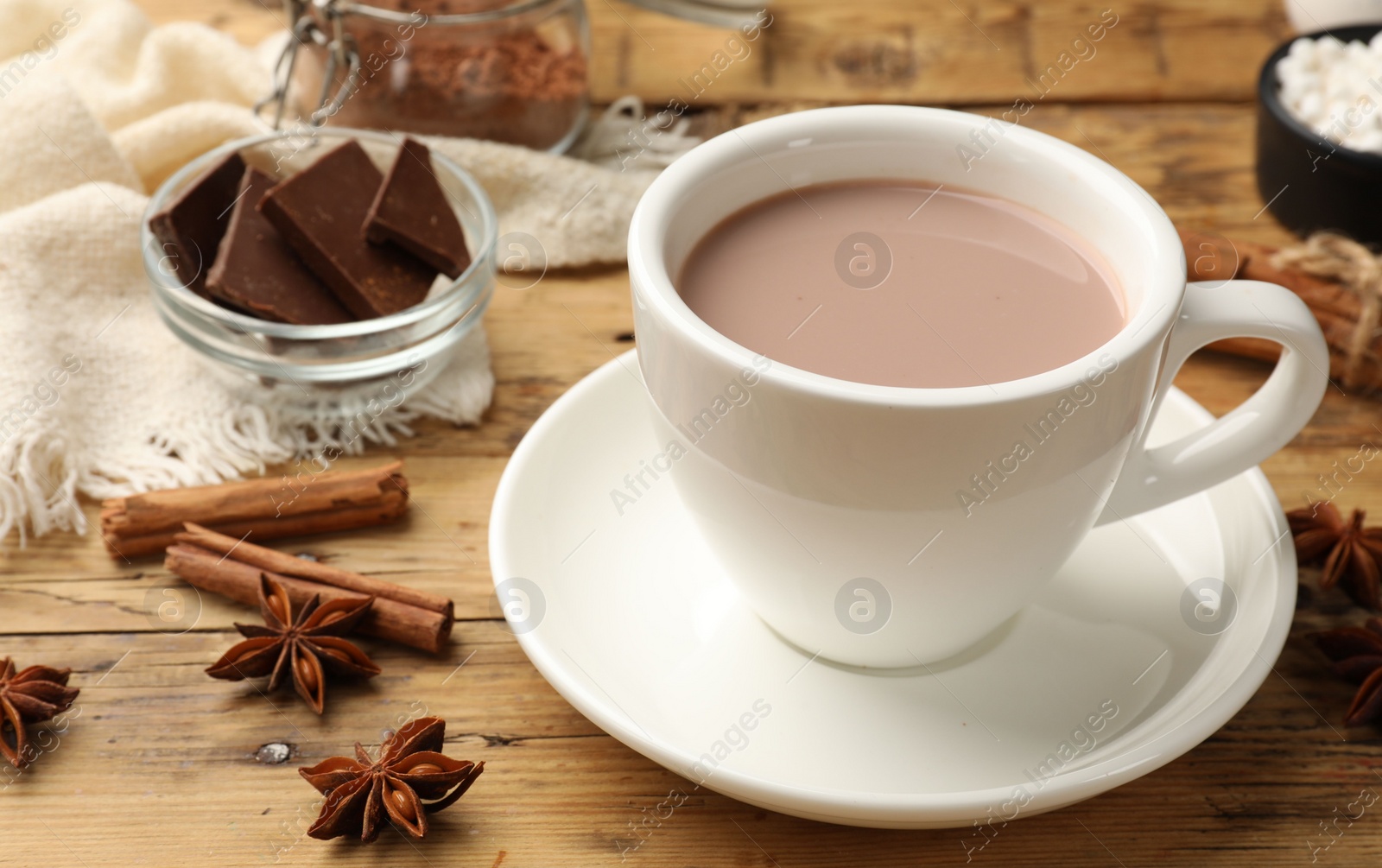 Photo of Tasty hot chocolate in cup and spices on wooden table, closeup