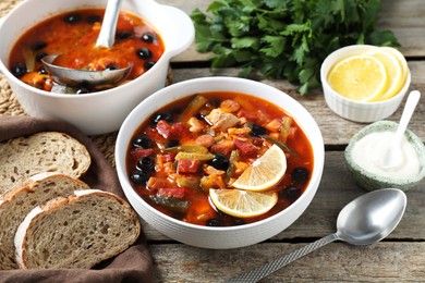 Meat solyanka soup with sausages, olives and vegetables served on wooden table