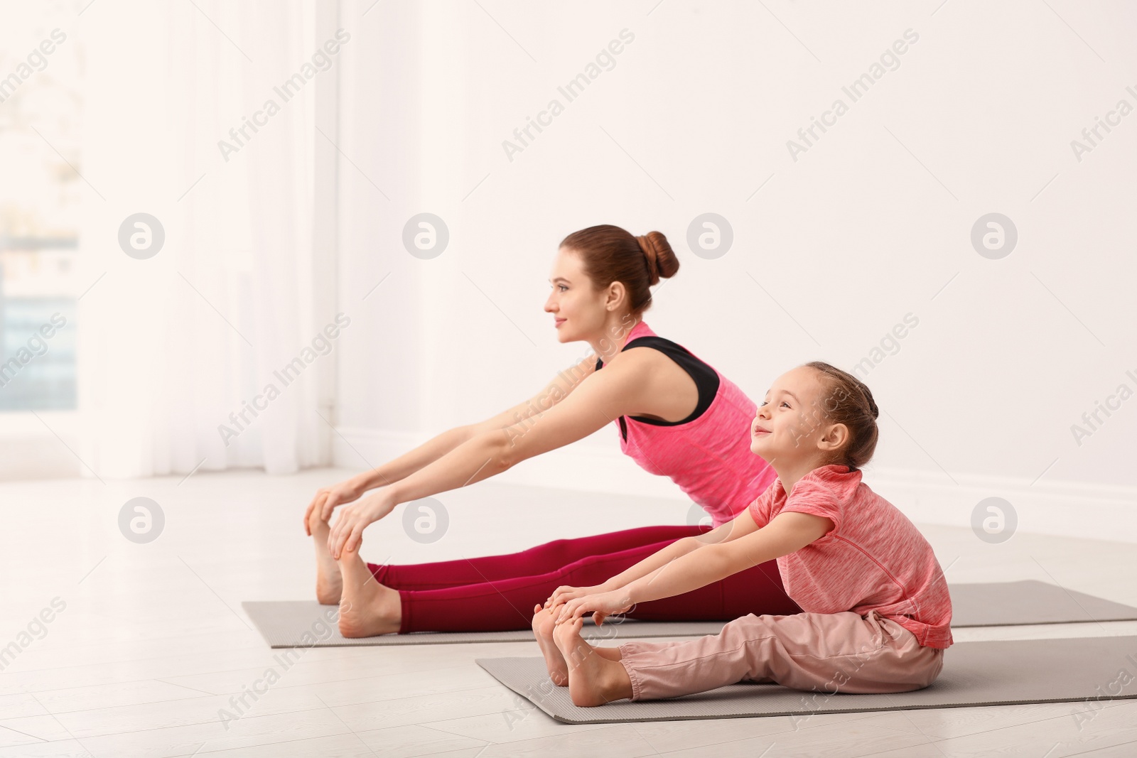 Photo of Young mother with little daughter practicing yoga at home