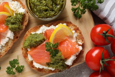 Photo of Delicious bruschettas with cream cheese, salmon and pesto sauce on light grey table, top view