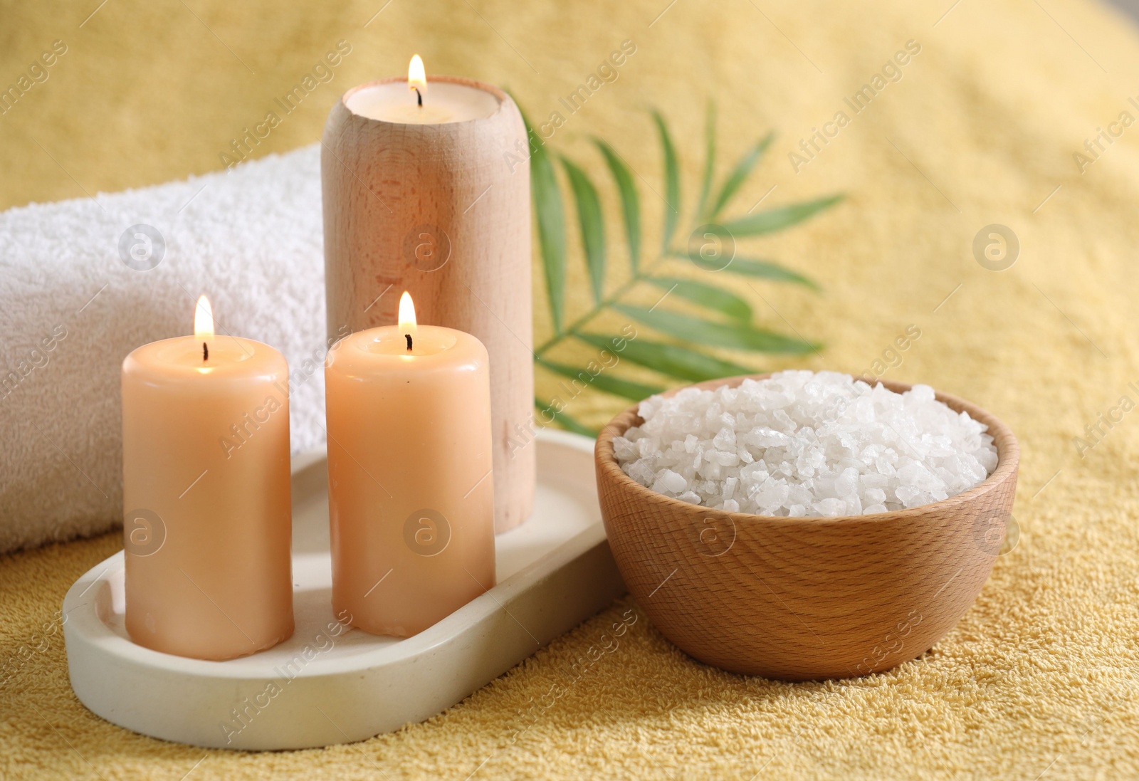 Photo of Spa composition. Burning candles, sea salt and towel on soft yellow fabric