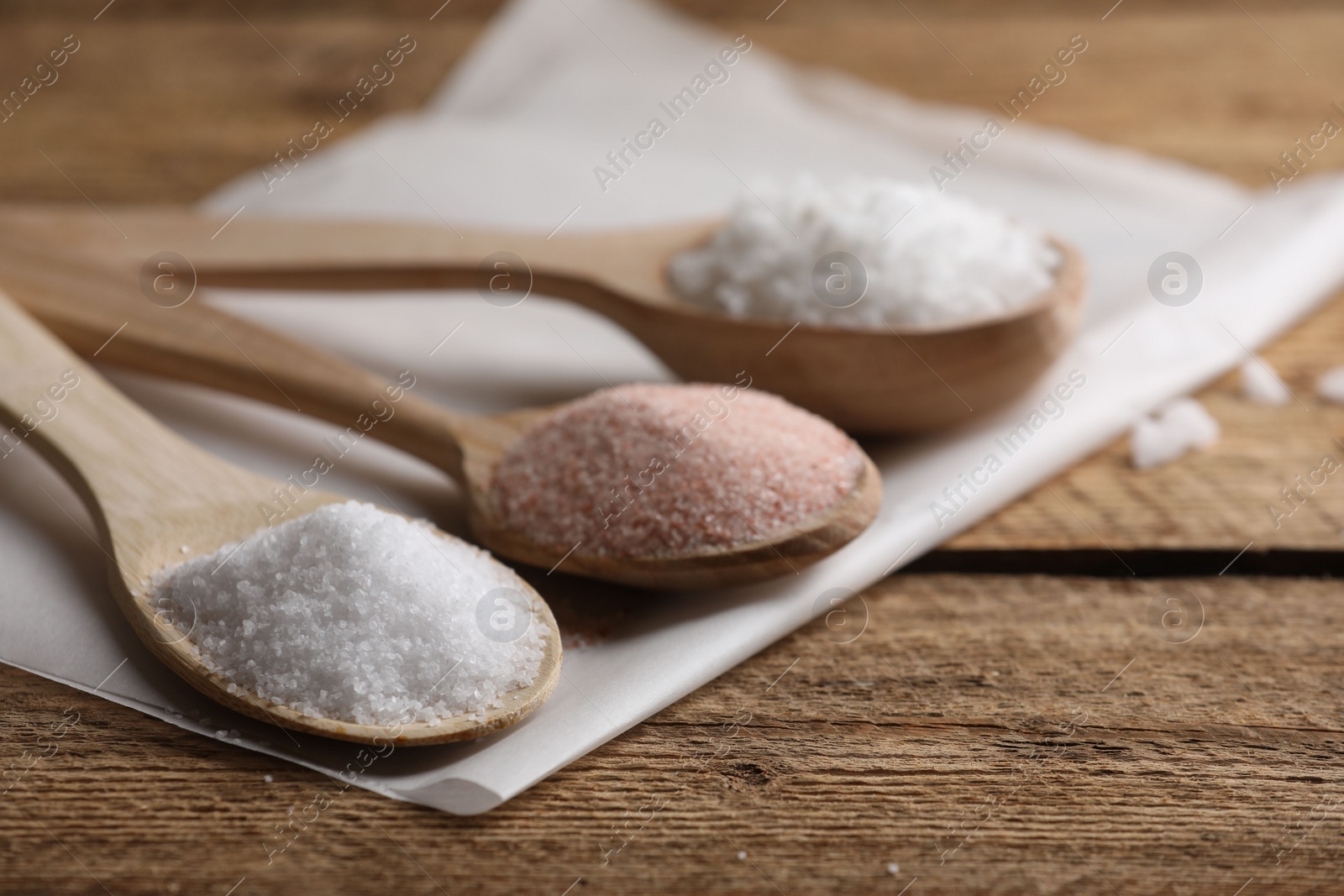 Photo of Different salt in spoons on wooden table, closeup