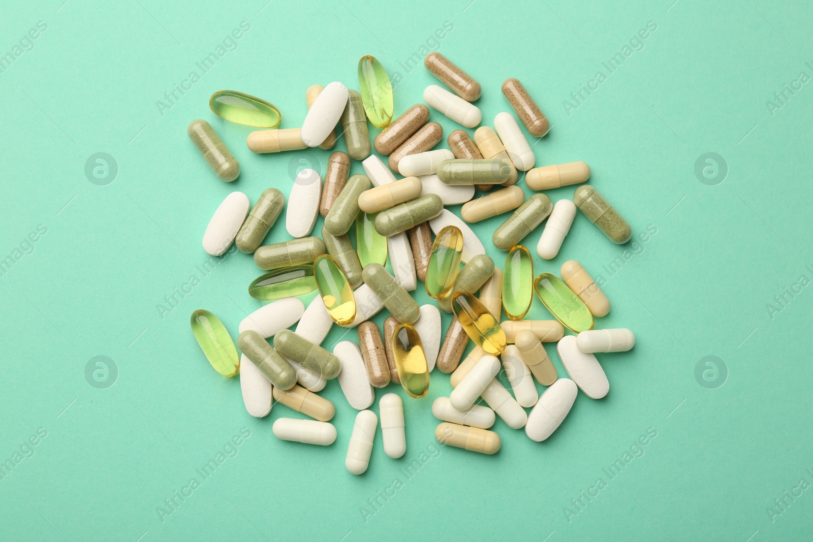 Photo of Different vitamin capsules on turquoise background, top view