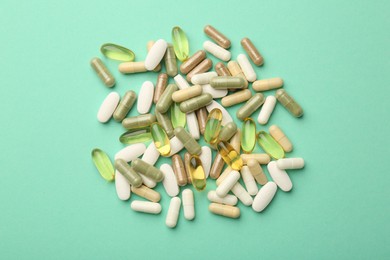 Photo of Different vitamin capsules on turquoise background, top view