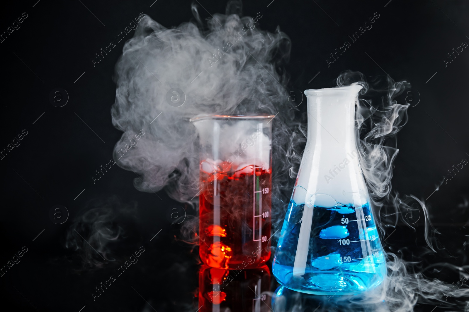 Photo of Laboratory glassware with colorful liquids and steam on black background. Chemical reaction