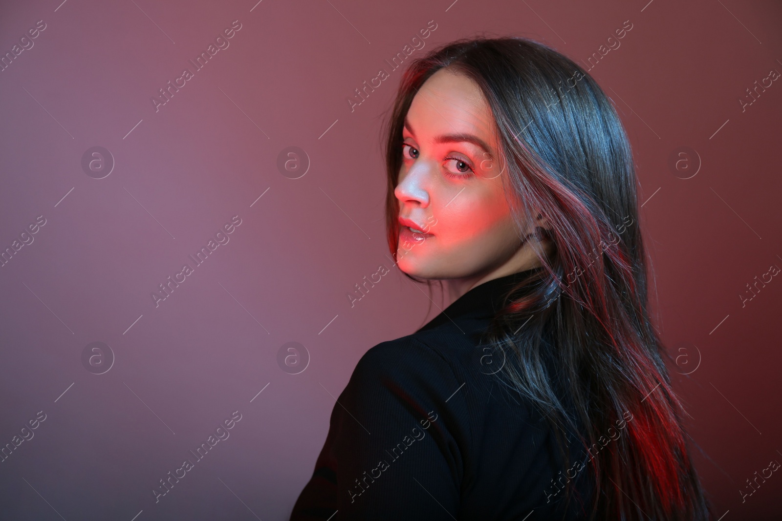 Photo of Portrait of beautiful young woman on color background with neon lights. Space for text