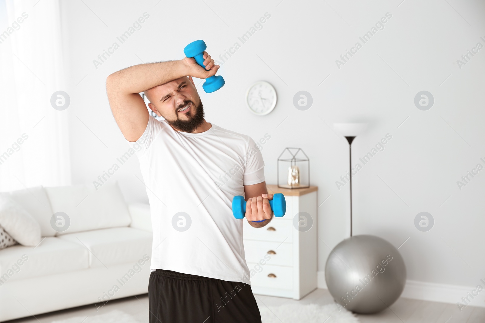 Photo of Tired overweight man doing exercise with dumbbells at home
