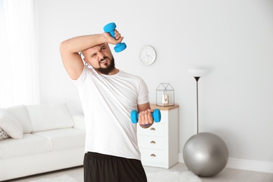 Tired overweight man doing exercise with dumbbells at home