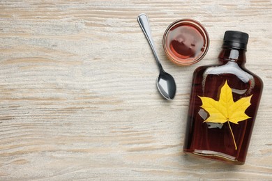 Photo of Tasty maple syrup and dry leaf on wooden table, flat lay. Space for text