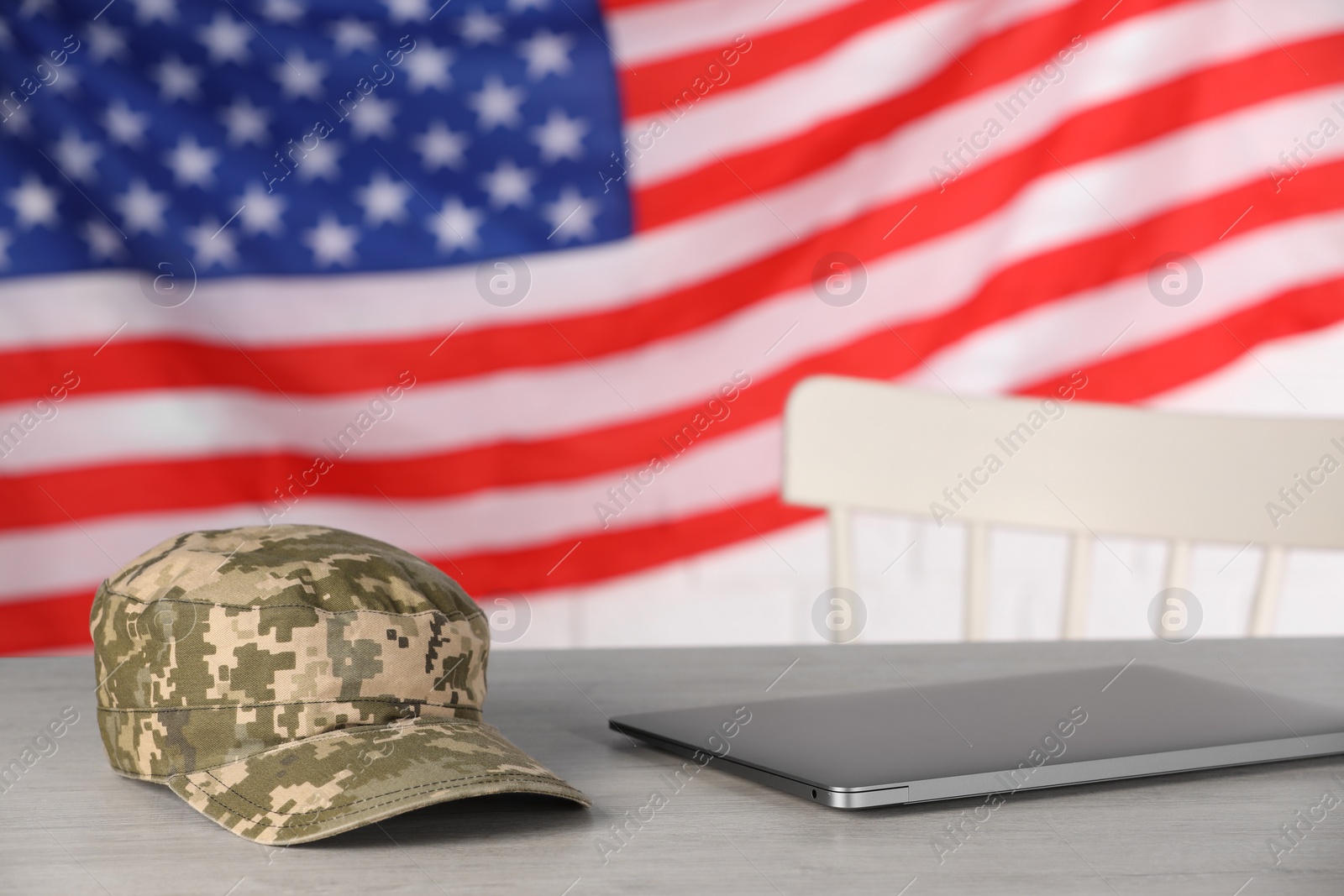 Photo of Cap and laptop on wooden table against flag of USA. Military education