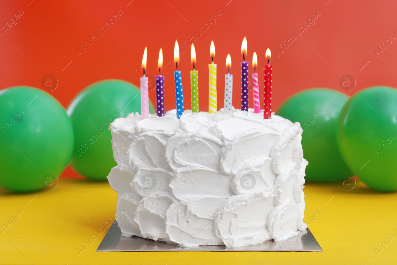 Photo of Delicious cake with burning candles and festive decor on yellow wooden table