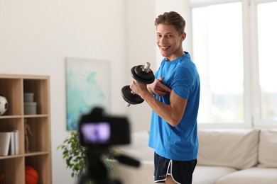 Photo of Smiling sports blogger working out with dumbbell while recording fitness lesson at home